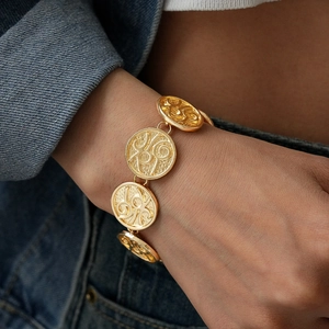Close-up of a gold metal coin bracelet with embossed textures worn on a wrist