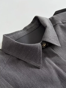 Gros plan du col de chemise gris foncé montrant la texture du sergé et les boutons assortis