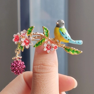 Detail of bird brooch with enamel berries and leaves held in hand for scale
