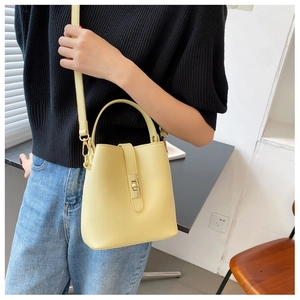 Detail shot of a beige PU leather bucket bag with metal clasp worn as a crossbody bag