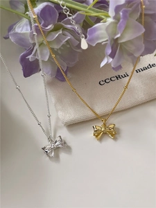Detailed view of silver and gold bow pendants on bead chains with a polished finish