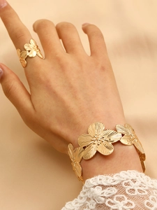 Detail view of gold floral textured ring and bracelet set worn on a beige fabric background