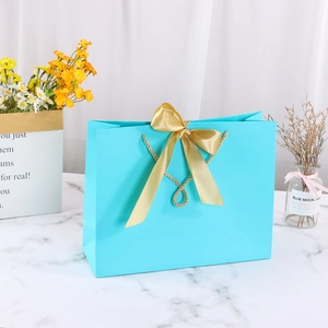 Elegant blue gift paper bag with golden ribbon bow on a minimalist marble surface