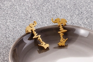 Detail of gold elephant earrings with heartbeat line design on grey ceramic surface