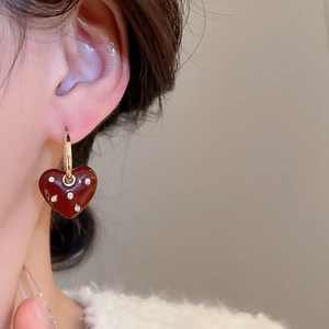 Close-up of a gold hoop earring with a red heart pendant and small sparkling stones
