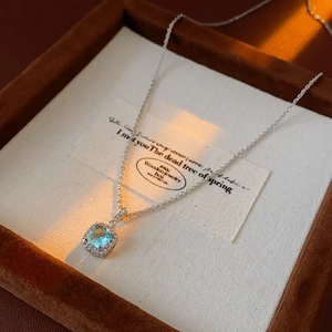 Macro shot of square blue zircon necklace on vintage brown velvet jewelry box with warm light