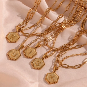 Detail of golden paperclip chain necklaces with hexagonal initial pendants on silk