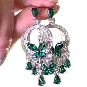 Silver drop earrings with green emerald gems and butterfly tassels held in hand