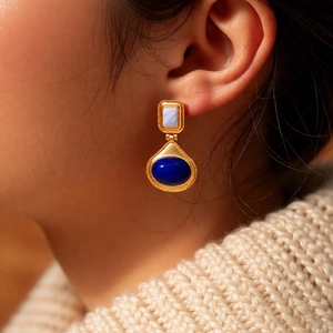 Detail of vintage gold oval earrings with deep blue gemstones worn with a cream sweater