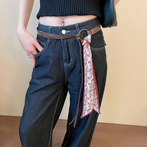 Detail of a brown leather belt with a red paisley silk scarf tassel on blue vintage jeans