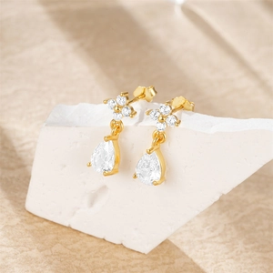 Macro shot of gold teardrop earrings with crystals on white stone background