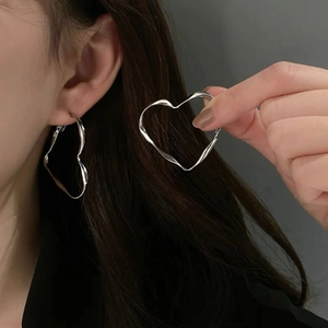 Detail of silver twisted heart earrings showing stylish metallic flow on model ear
