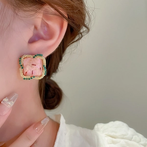 Détail de boucles d'oreilles carrées en résine rose avec bordure dorée et cristaux