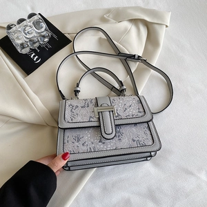 Detail view of grey leather handbag featuring textured floral lace and metal clasp