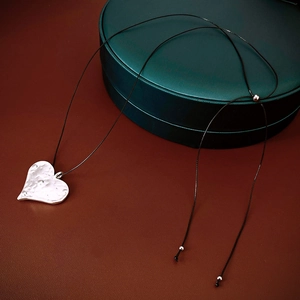 Close-up of heart-shaped silver pendant with hammered texture on black cord