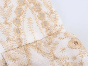 Macro shot of white cotton fabric with gold geometric embroidery and eyelet details