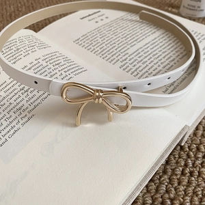 Close-up of a white vintage leather belt with a golden bow buckle on a classic book