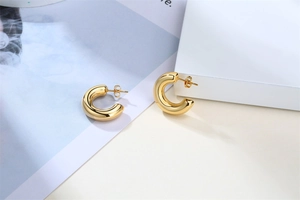 Detailed view of chunky golden C-shaped hoop earrings on a minimalist geometric background