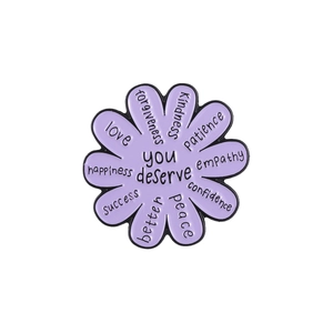 Detailed view of flower-shaped purple enamel pin with you deserve inspirational text