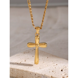 Détail du pendentif croix en acier doré 18 carats sur un socle en pierre texturée