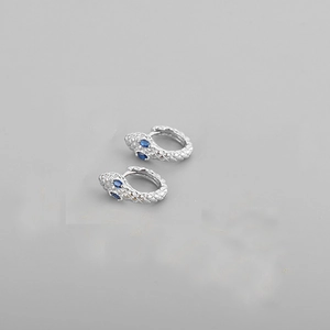 Close-up of silver snake earrings featuring sparkling blue gemstone eyes for a luxury look