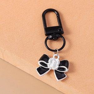 Detail of a black bow keychain featuring a delicate white rose charm on a soft base