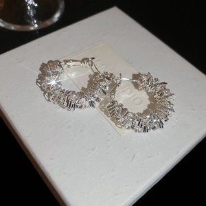 Close-up of irregular silver hoop earrings with sparkling pavé crystals on a gift box