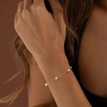 Gros plan d'un bracelet chaîne plaqué or avec petites perles blanches sur le poignet
