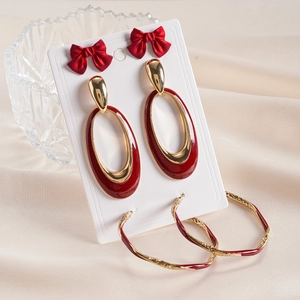 Close-up of six-piece set with red enamel bows and golden oval earrings on silk