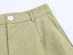 Detailed close-up of light green linen pants waist showing white button and fabric texture