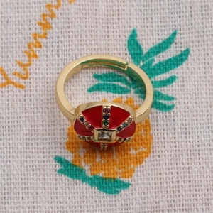 Détail macro d'une bague ajustable dorée avec émail rouge et motif en croix de zircon