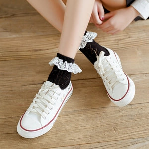 Women's black cotton socks with white lace ruffle trim shown on feet with white shoes