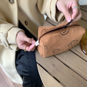 Close-up of brown corduroy cosmetic bag featuring smiley prints and smooth zipper closure