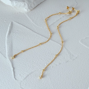 Macro detail of gold long chain tassel earrings with tiny beads and white opal gems