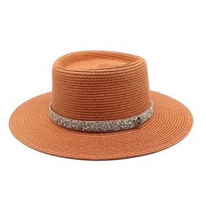 Detailed view of the woven brown straw hat featuring rhinestone band and 'M' metal plaque