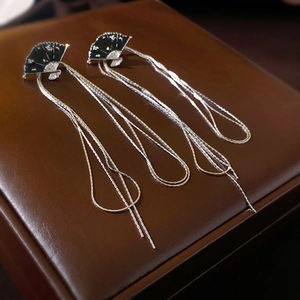 Detailed close-up of fan-shaped tassel earrings with black enamel on brown leather