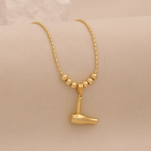Détail d'un collier doré avec pendentif sèche-cheveux et perles sur la chaîne