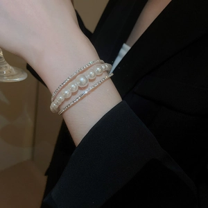Detail of layered bracelet with white pearls and silver rhinestones on a black suit
