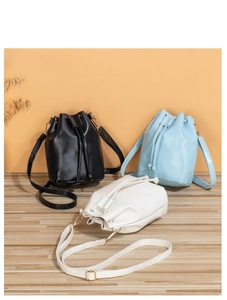Three mini drawstring bucket bags in black, light blue, and white on a wooden surface