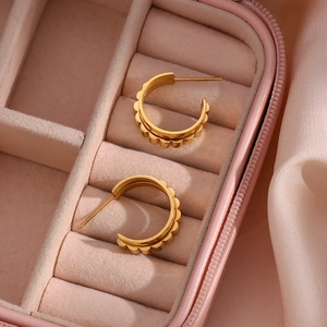Detailed macro view of gold-plated C-shaped gear earrings in a pink velvet jewelry box
