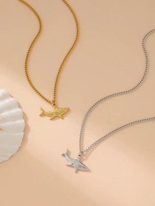 Close-up of gold and silver shark pendant necklaces on a shell and apricot background