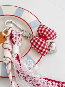Detail van rood-witte geblokte strik sleutelhanger met hartvormige hanger en kant
