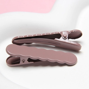 Close-up of wavy metal hair clips in dark purple lacquer finish on a white plate