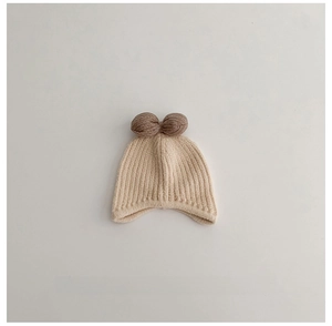 Detail of baby knitted earflap hat with brown pom-poms and ribbed edges in cream white