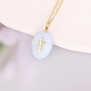 Detailed macro view of a light blue teardrop pendant with golden cross on a gold chain