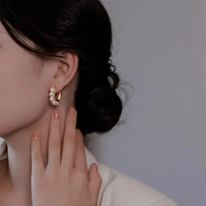 Détail des boucles d'oreilles C dorées avec cinq perles blanches portées par un mannequin