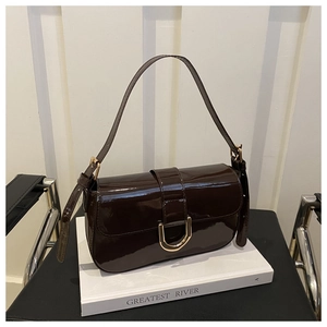 Close-up of glossy patent leather bag with gold U-shaped buckle on white book display