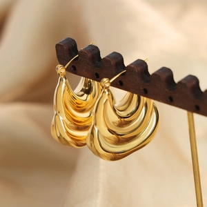 Gold chunky pleated croissant hoop earrings in polished titanium steel on a wood stand