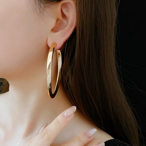 Close-up of model wearing large golden oval hoop earrings against a dark background