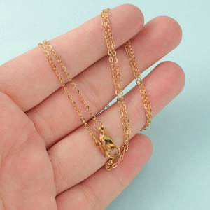 Detailed view of a thin golden stainless steel necklace with lobster clasp on a palm